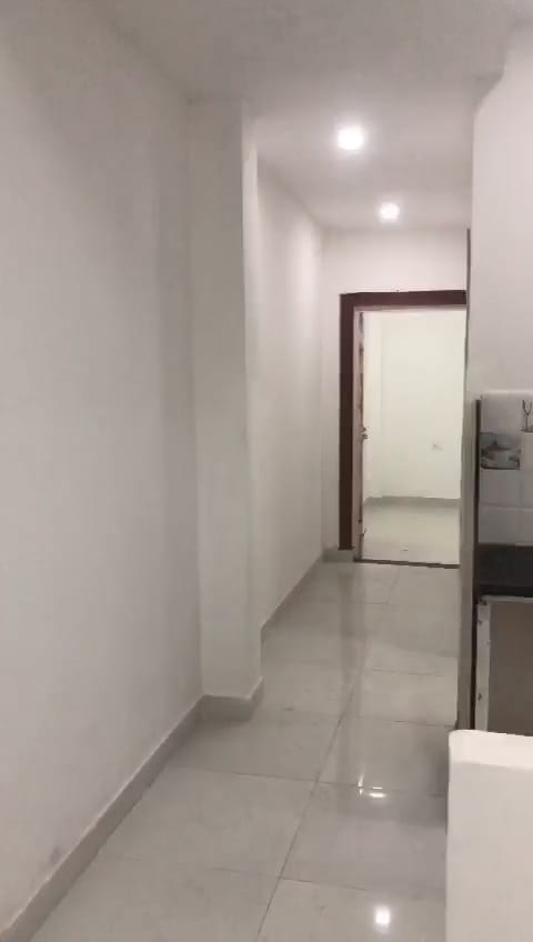 Corridor with glossy floor tiles and white walls leading to a doorway.