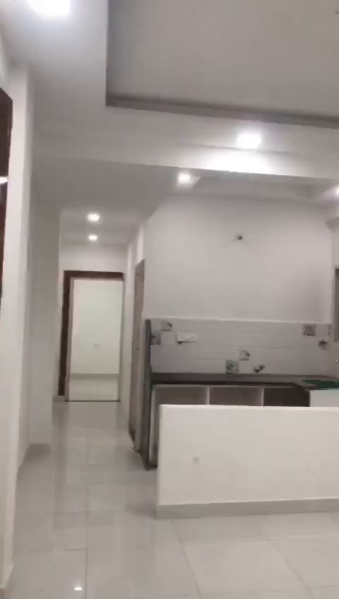 Finished flat: open hall with a false ceiling and recessed lights, leading to a kitchen platform with tiled backsplash.